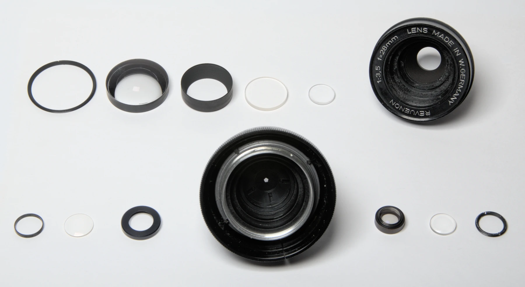 Éléments réels d’un objectif Revuenon 28 mm démonté, disposés pour la photographie ; cette vue ne mesure pas sa diffusion.